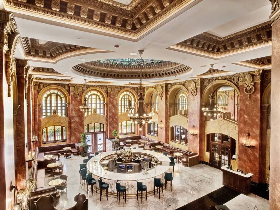A grand lobby with a central bar, arched windows, and ornate ceiling details.