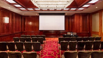 A conference room with rows of chairs, a large screen, and a chandelier.