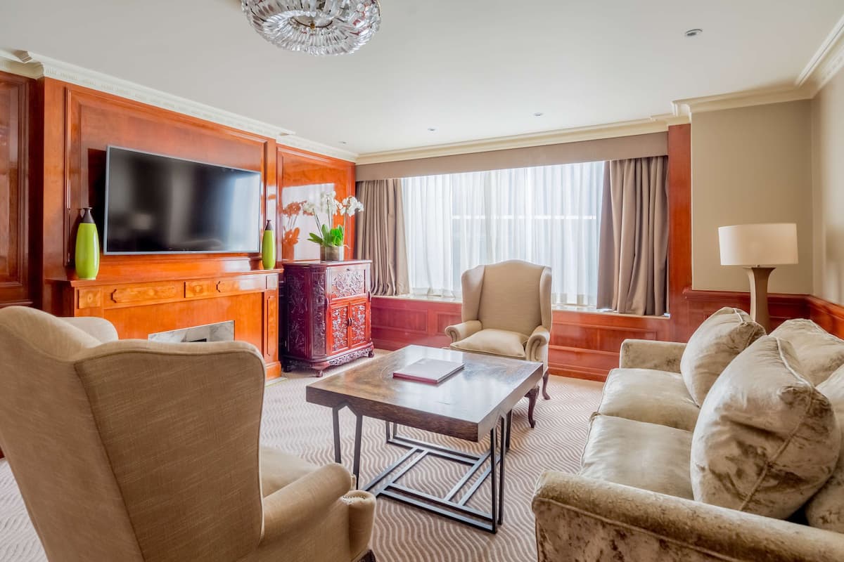 A hotel room with a flat-screen TV, a wooden cabinet, a red decorative piece, a beige armchair, a white sofa, and a lamp.