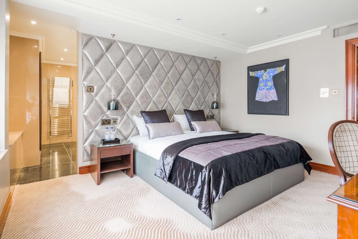 A modern bedroom with a large bed, a headboard with a diamond pattern, a bedside table with a lamp, and a framed artwork on the wall.