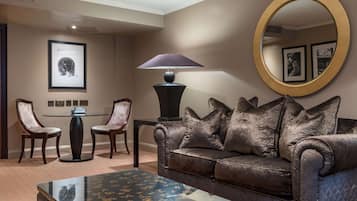 A room with a leather sofa, a round mirror, a table with chairs, and a lamp.