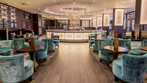 A modern bar area with a central bar counter, seating with round tables and chairs, and a decorative chandelier. - Radisson Blu Hotel, London Heathrow (Hayes)