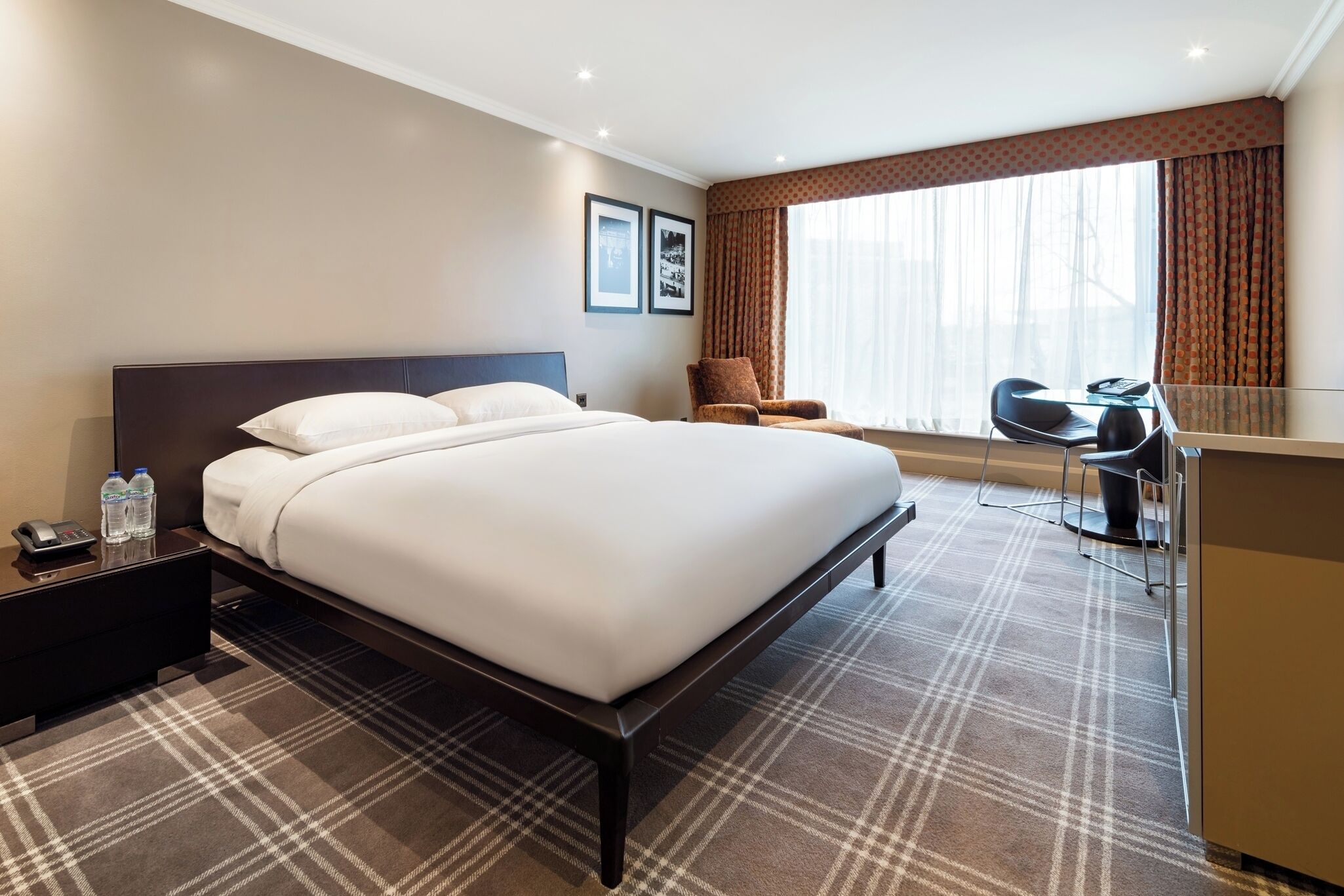Una habitación de hotel con una cama grande, un escritorio, una silla y un ventanal con cortinas.