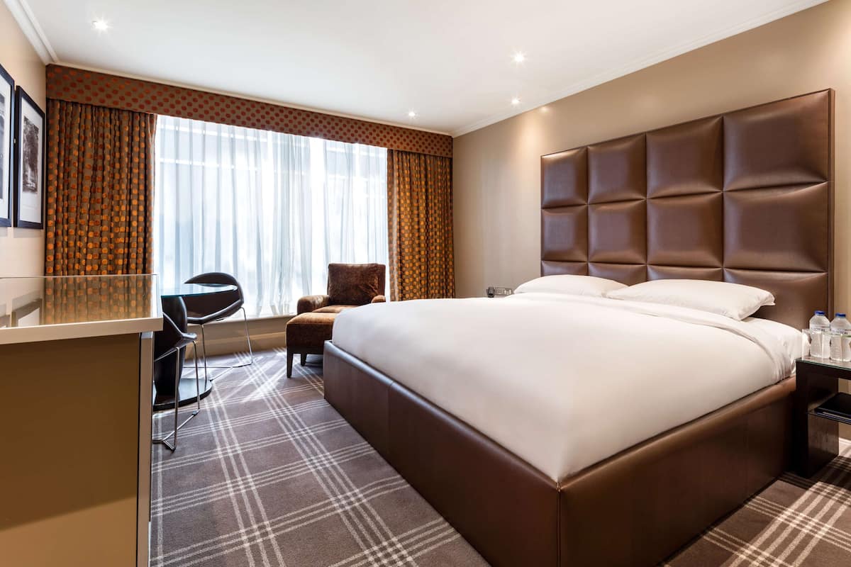 A hotel room with a large bed, a desk, a chair, and a window with curtains.