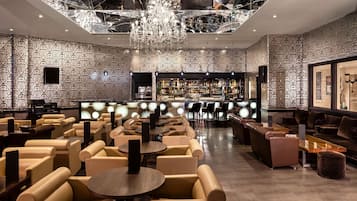 A modern bar area with a patterned wall, a chandelier, and seating arrangements.