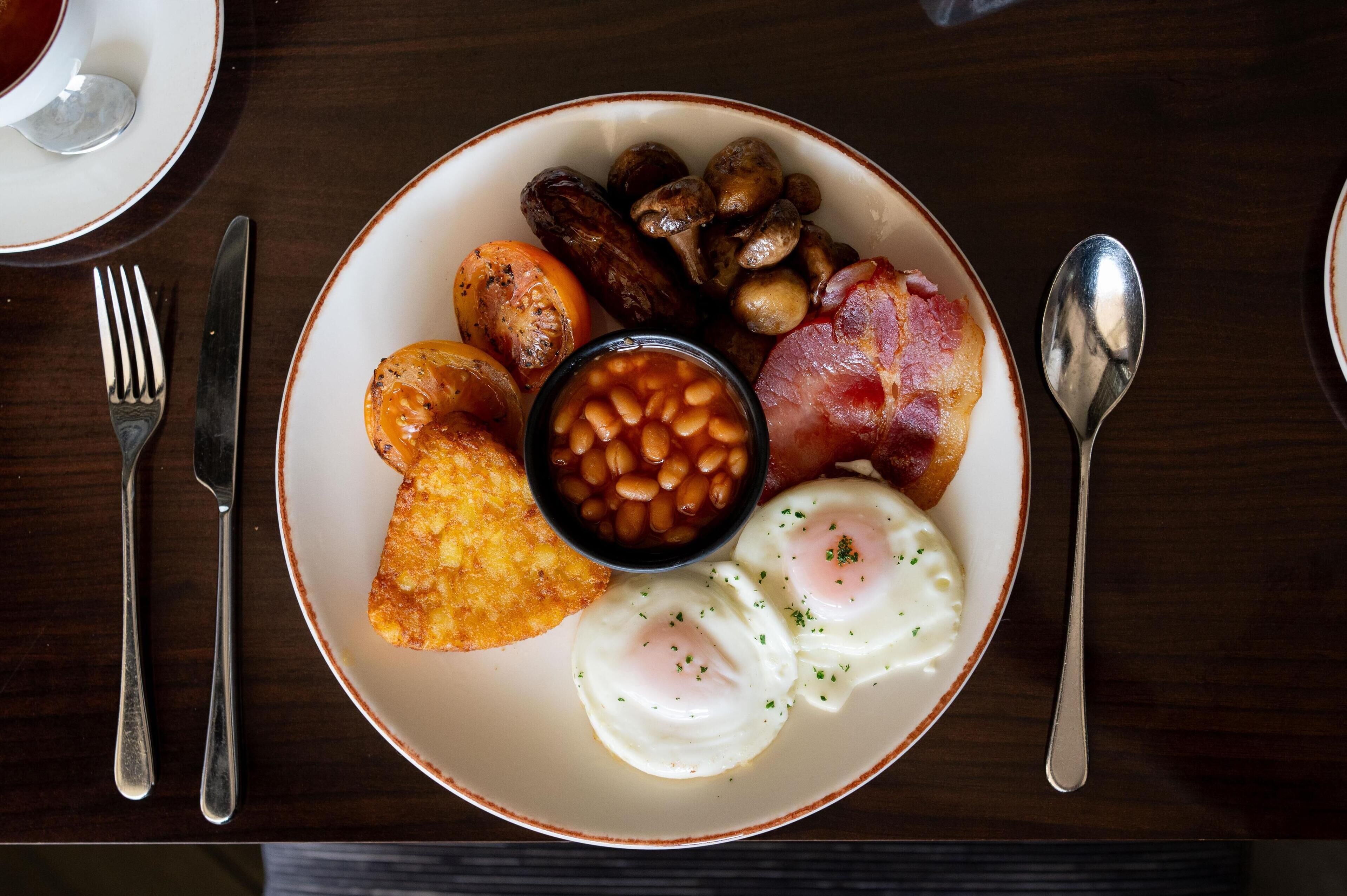 A plate of breakfast food including eggs, beans, bacon, sausages, and toast.