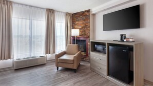 A hotel room with a flat-screen TV, a sofa, a fireplace, a mini-fridge, and a large window with curtains. - Quality Inn & Suites (Niagara Falls)