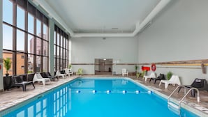 An indoor swimming pool with clear views through large windows, a poolside lounge area, and a visible exit door. - Quality Inn & Suites (Niagara Falls)