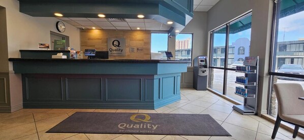 A hotel reception area with a blue counter, a clock, an ATM, and a Red Bull vending machine. - Quality Inn & Suites (Niagara Falls)