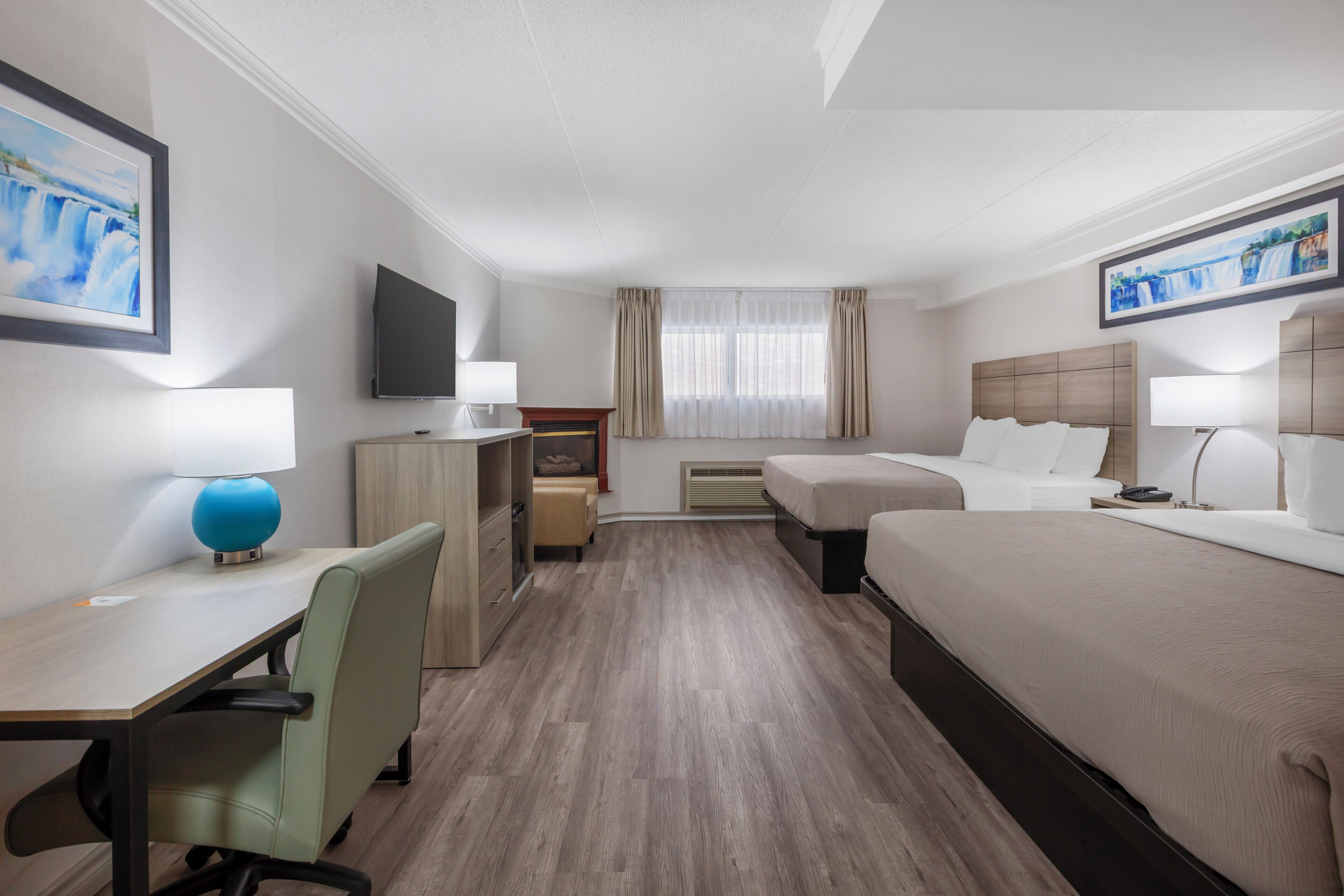 A hotel room with a desk, two beds, a TV, and artwork on the walls.