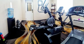 A gym with exercise equipment including a stationary bike, elliptical, and treadmill. There are dumbbells and a water bottle on the floor. - Quality Inn & Suites (Niagara Falls)