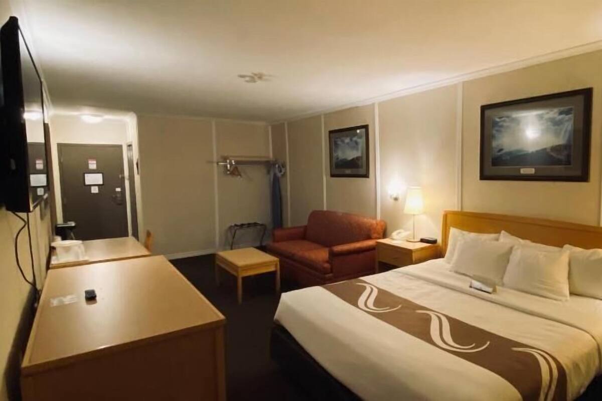 A hotel room with a bed, a desk, a chair, a TV, and a door.