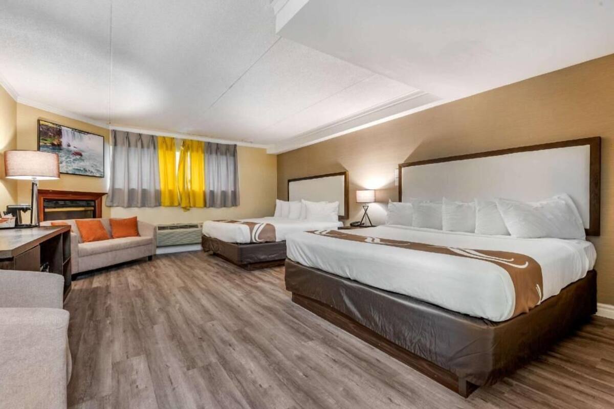 A hotel room with a large bed, two bedside tables, a desk, a chair, a sofa, and a window with curtains.