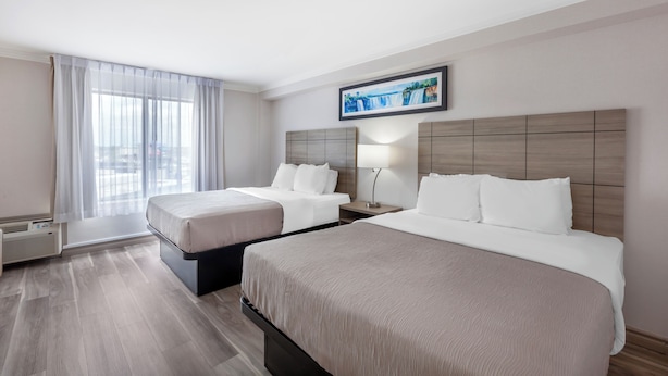 A hotel room with two beds, a large window with sheer curtains, a framed picture on the wall, and a modern design. - Quality Inn & Suites (Niagara Falls)