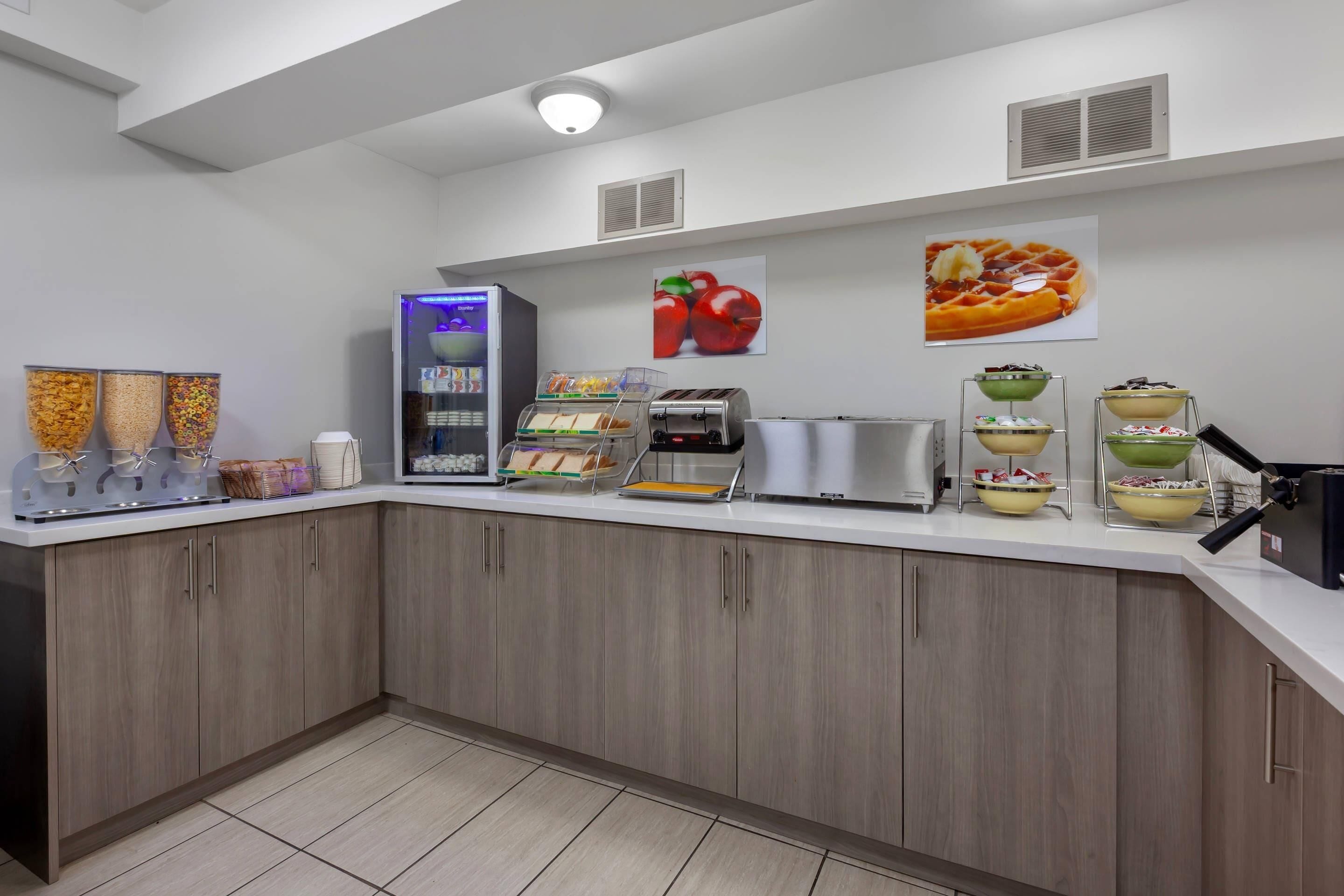 A modern kitchen with a self-serve station, a waffle maker, and a fruit display.