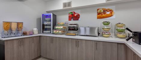 A modern kitchen with a self-serve station, a waffle maker, and a fruit display.