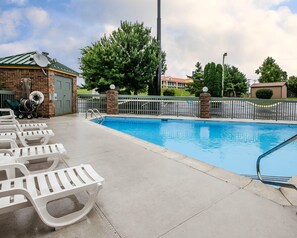 A swimming pool with lounge chairs, a brick building, and a fenced area with trees.