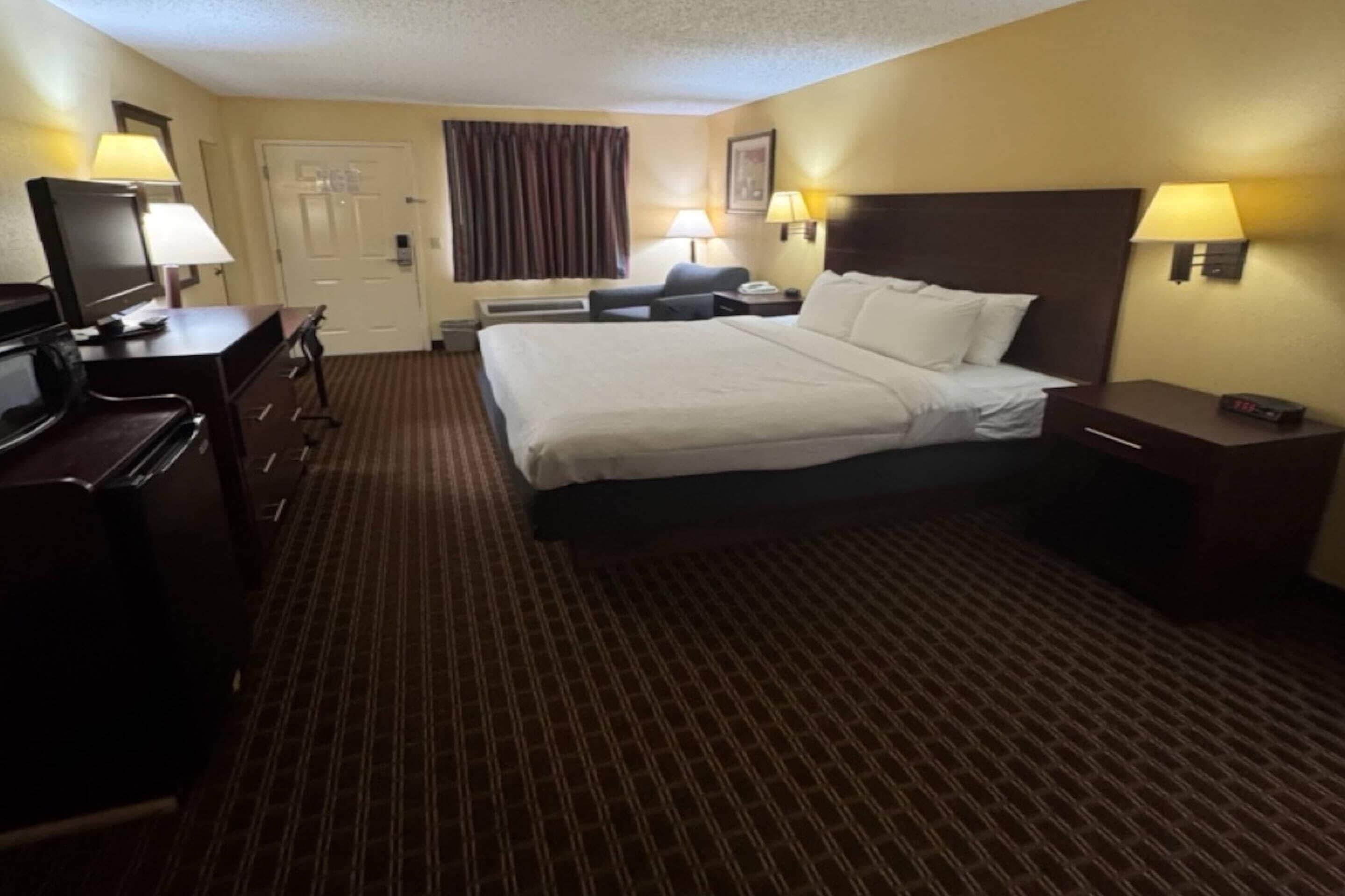 Une chambre d’hôtel avec un lit, un bureau, une chaise, une télévision, des lampes et une porte.