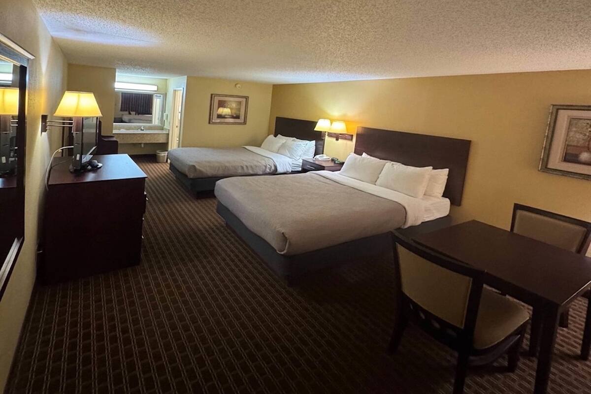 A hotel room with two beds, a desk with a chair, a lamp, and a small table.