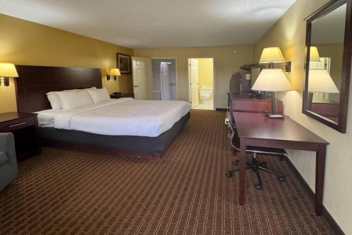 A hotel room with a bed, desk, chair, lamp, and a mirror.