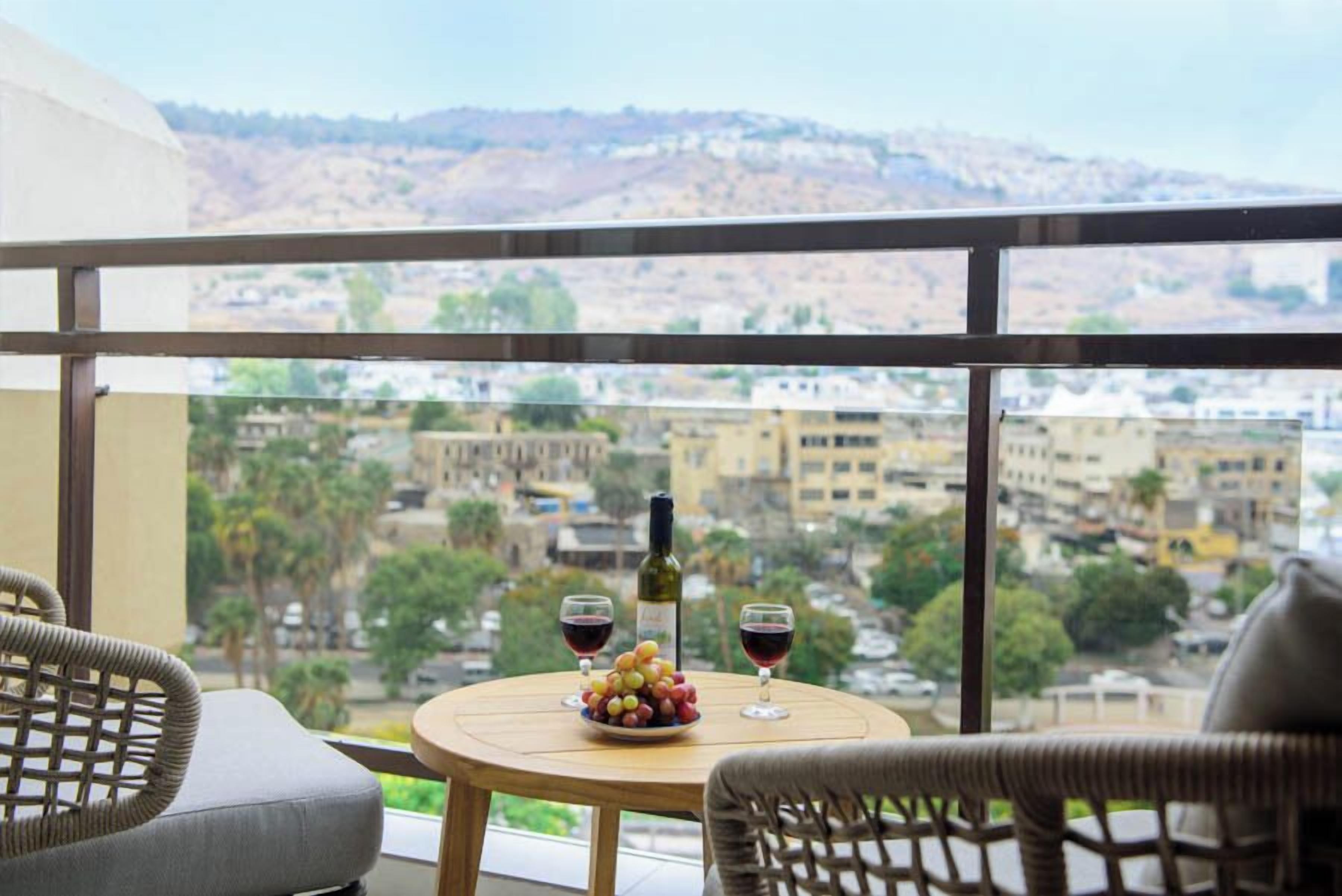 Ein Balkon mit Korbstühlen, einem runden Tisch, einer Weinflasche und Gläsern, mit Blick auf eine Stadtlandschaft.