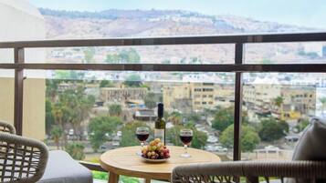 Ein Balkon mit Korbstühlen, einem runden Tisch, einer Weinflasche und Gläsern, mit Blick auf eine Stadtlandschaft.