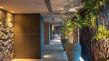 A hallway with stone walls, large planters, and a view into a room with a bed and a stone wall.