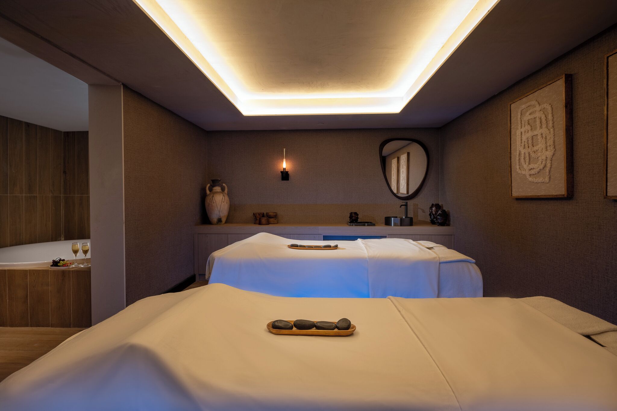 A modern bedroom with a large bed, a bedside table, a mirror, and a wall-mounted light fixture.