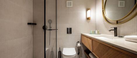 Un baño moderno con ducha acristalada, inodoro, lavabo con tocador de madera y un espejo grande.