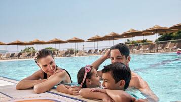 Una piscina con sillones de descanso y sombrillas al fondo.