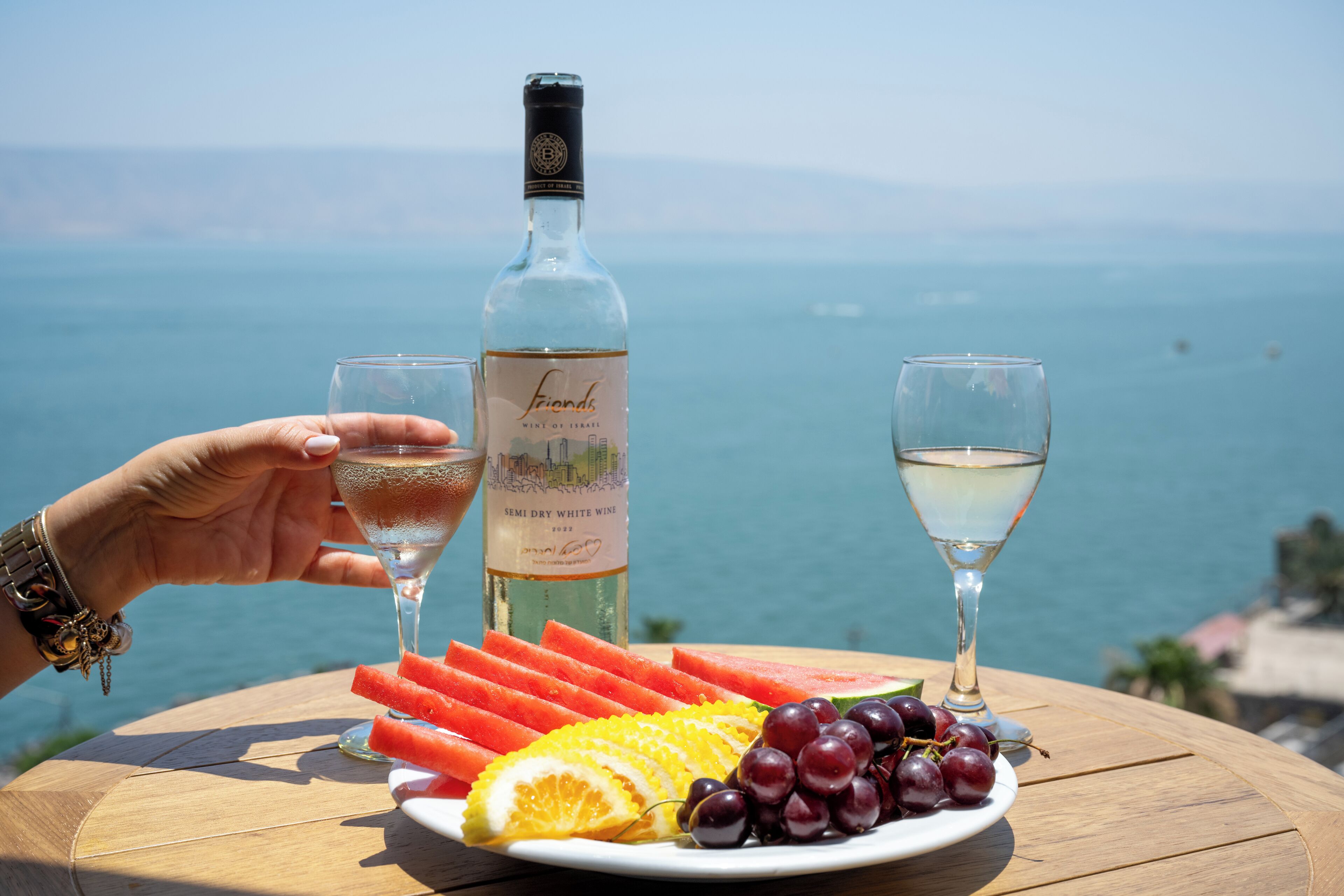 A table with a bottle of wine, two glasses, and a plate of fruit.