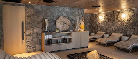 Un área de spa con pared de piedra, un mueble de madera con artículos de tocador y sillones de descanso.