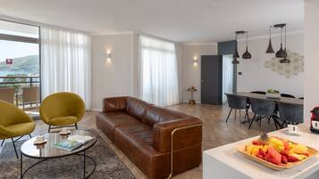 A modern living room with a brown leather sofa, yellow armchairs, and a glass coffee table. A dining area with a white table and chairs is visible in the background.