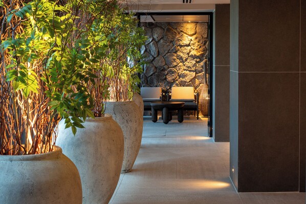 A hallway with large potted plants, a stone wall, and a seating area with a table and chairs. - Leonardo Plaza Kinneret (Tiberias)