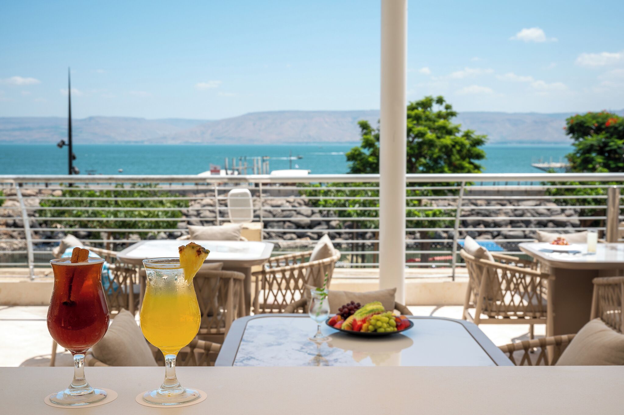 Une terrasse avec une table, deux boissons et un panier de fruits.