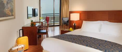 A hotel room with a bed, a desk with a chair, a television, and a window with a view.