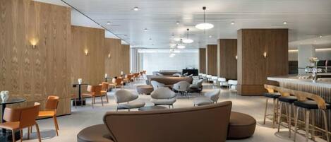 A spacious, modern lounge area with a central seating area, multiple tables, and bar stools.