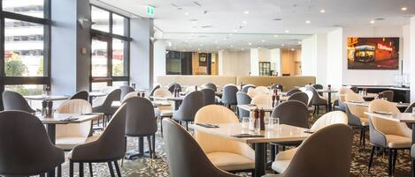 A spacious restaurant with multiple tables and chairs, large windows, and a modern interior design.
