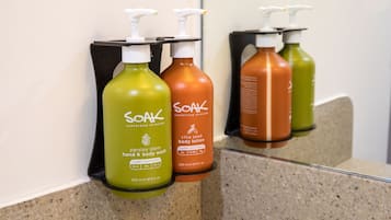 A bathroom with a granite countertop and three bottles of Soak body lotion on a black soap dispenser holder.
