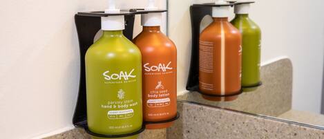 A bathroom with a granite countertop and three bottles of Soak body lotion on a black soap dispenser holder.