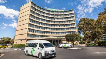 Um edifício de hotel curvo com uma placa verde, uma van e um carro estacionados na frente.