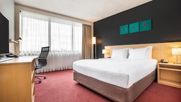 Una habitació d'hotel amb un llit gran, un escriptori amb una cadira, una làmpada d'escriptori i una tauleta de nit amb una làmpada.