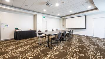 Une salle de conférence avec une longue table, des chaises, un écran de projection et un sol recouvert de moquette.