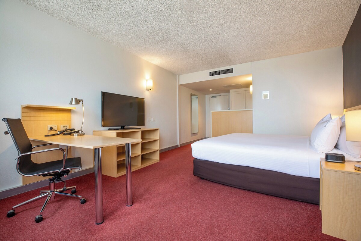 Une chambre d’hôtel équipée d’un lit, d’un bureau, d’une chaise, d’une télévision et d’une petite table de chevet.