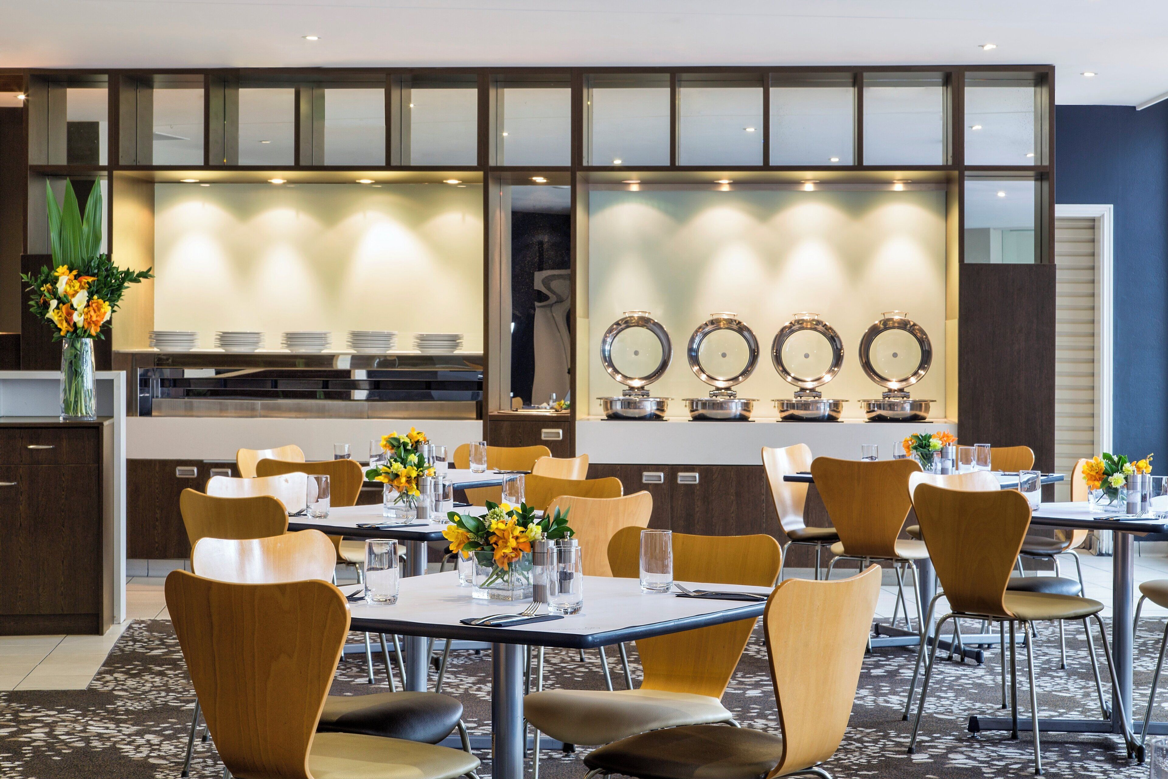 Un espace repas moderne avec des tables et des chaises, un buffet et des miroirs décoratifs fixés aux murs.