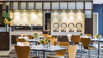 Un espace repas moderne avec des tables et des chaises, un buffet et des miroirs décoratifs fixés aux murs.