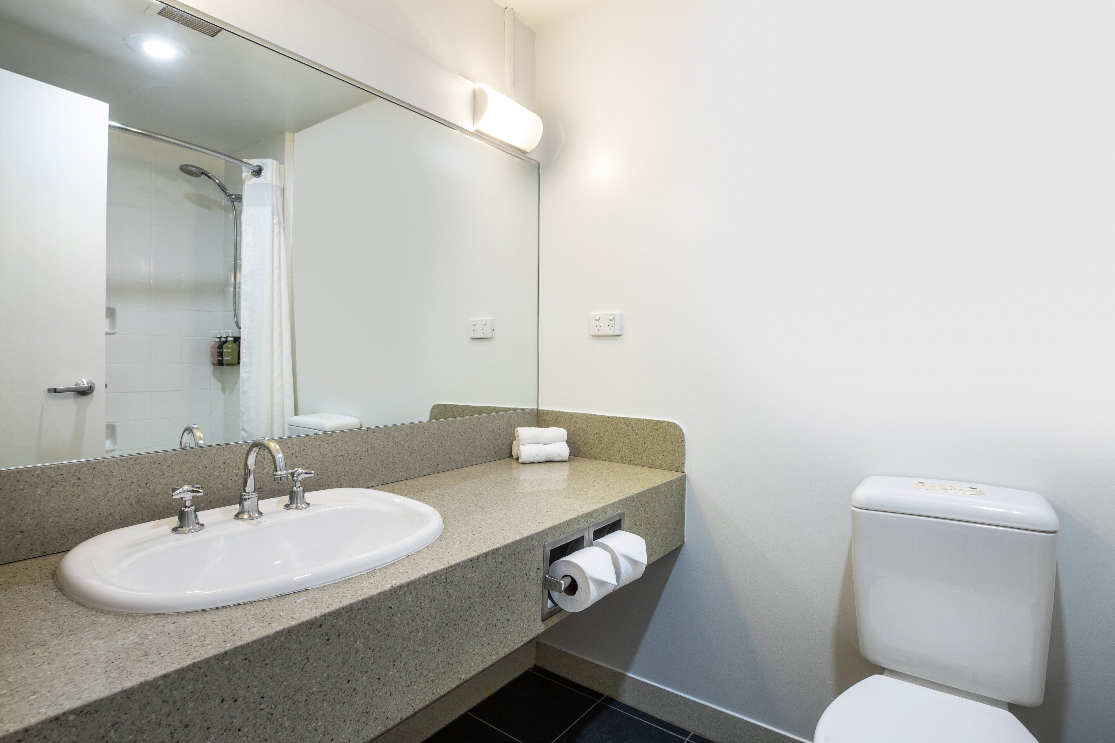 A bathroom with a sink, mirror, toilet, and shower.