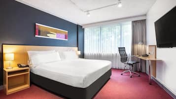Una habitación de hotel con una cama grande, un escritorio con silla, un televisor y una ventana con cortinas.