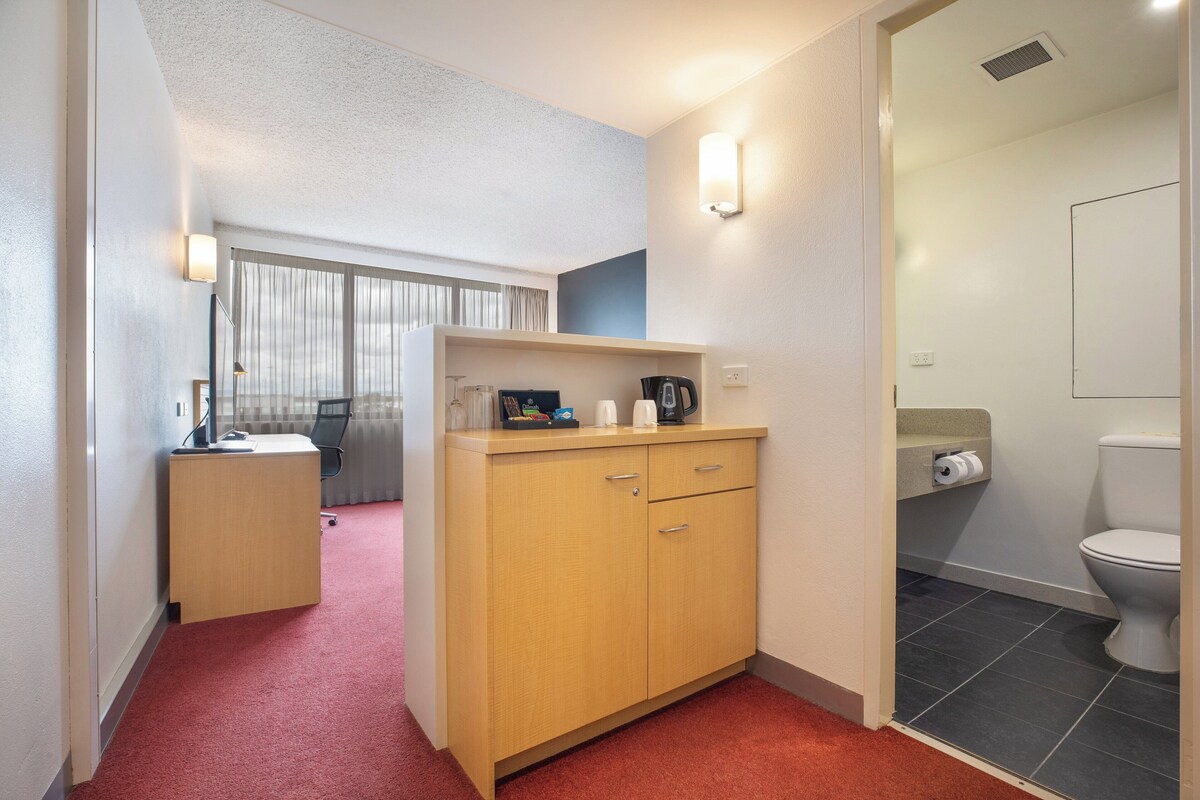 Une chambre d’hôtel compacte comprenant un bureau, une petite kitchenette, des toilettes et un espace douche.