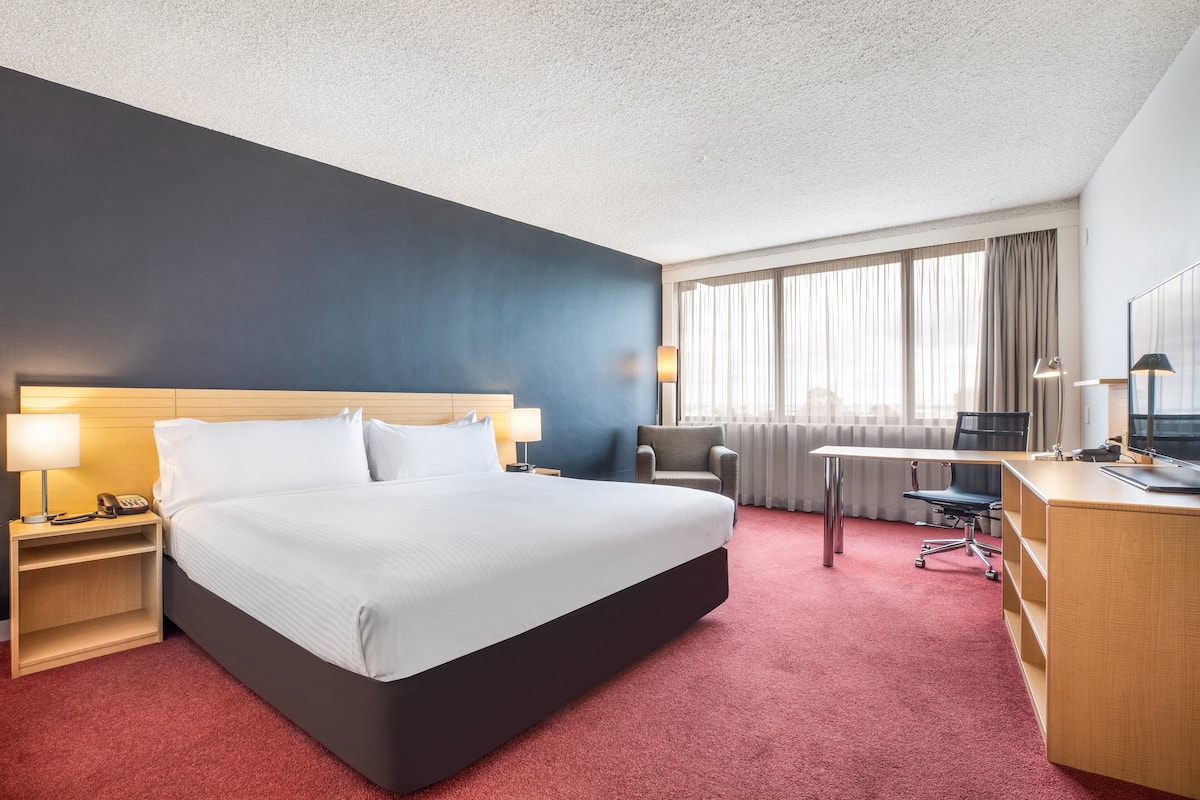 A hotel room with a large bed, a desk, a chair, and a window with curtains.